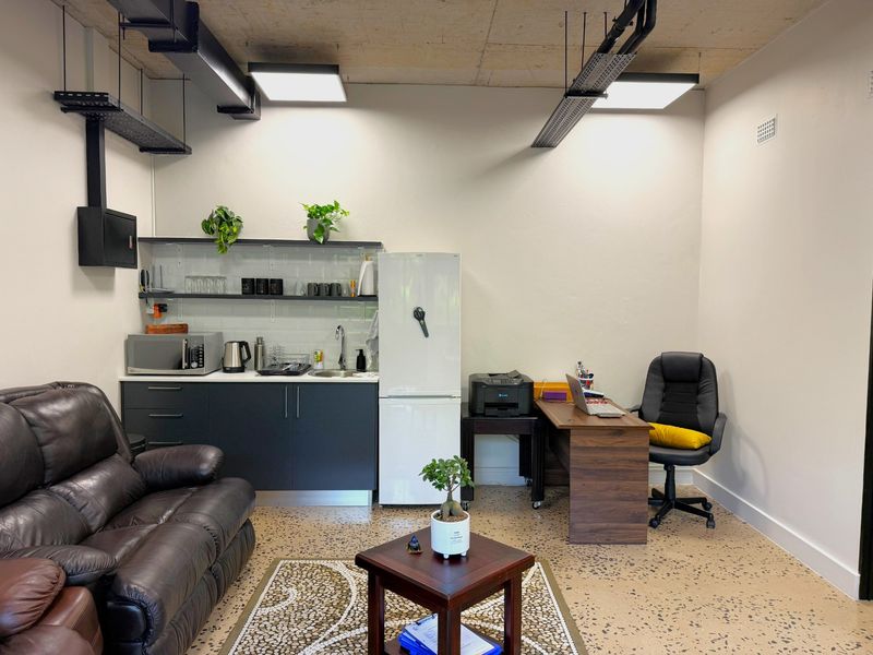 Modern office space featuring polished concrete floors, exposed industrial ceiling with cable trays, and a compact built-in kitchenette with subway tile backsplash.