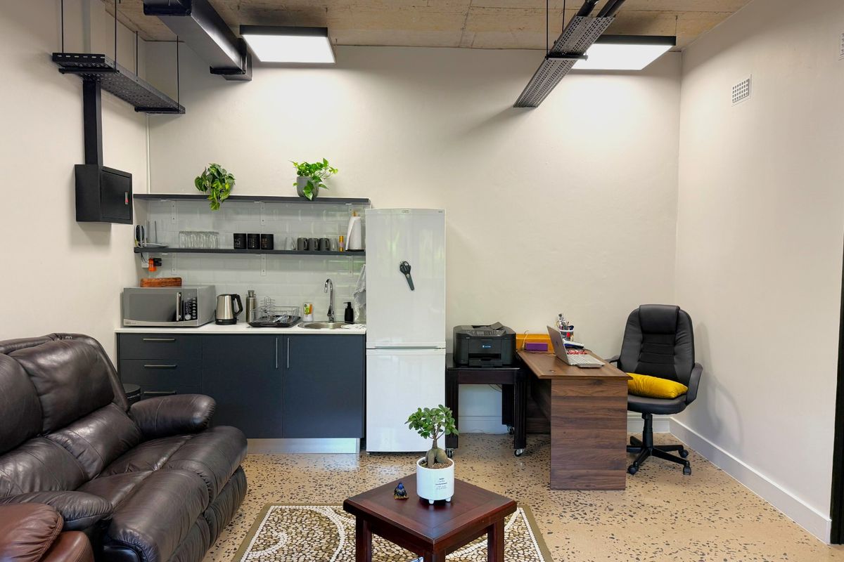 Modern office space featuring polished concrete floors, exposed industrial ceiling with cable trays, and a compact built-in kitchenette with subway tile backsplash.