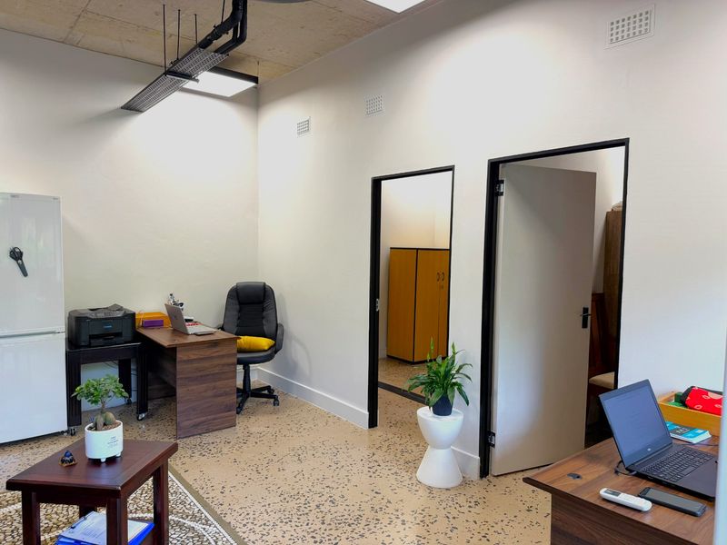 A modern office space featuring exposed concrete ceilings, durable terrazzo flooring, and clean white walls with contrasting black door frames.