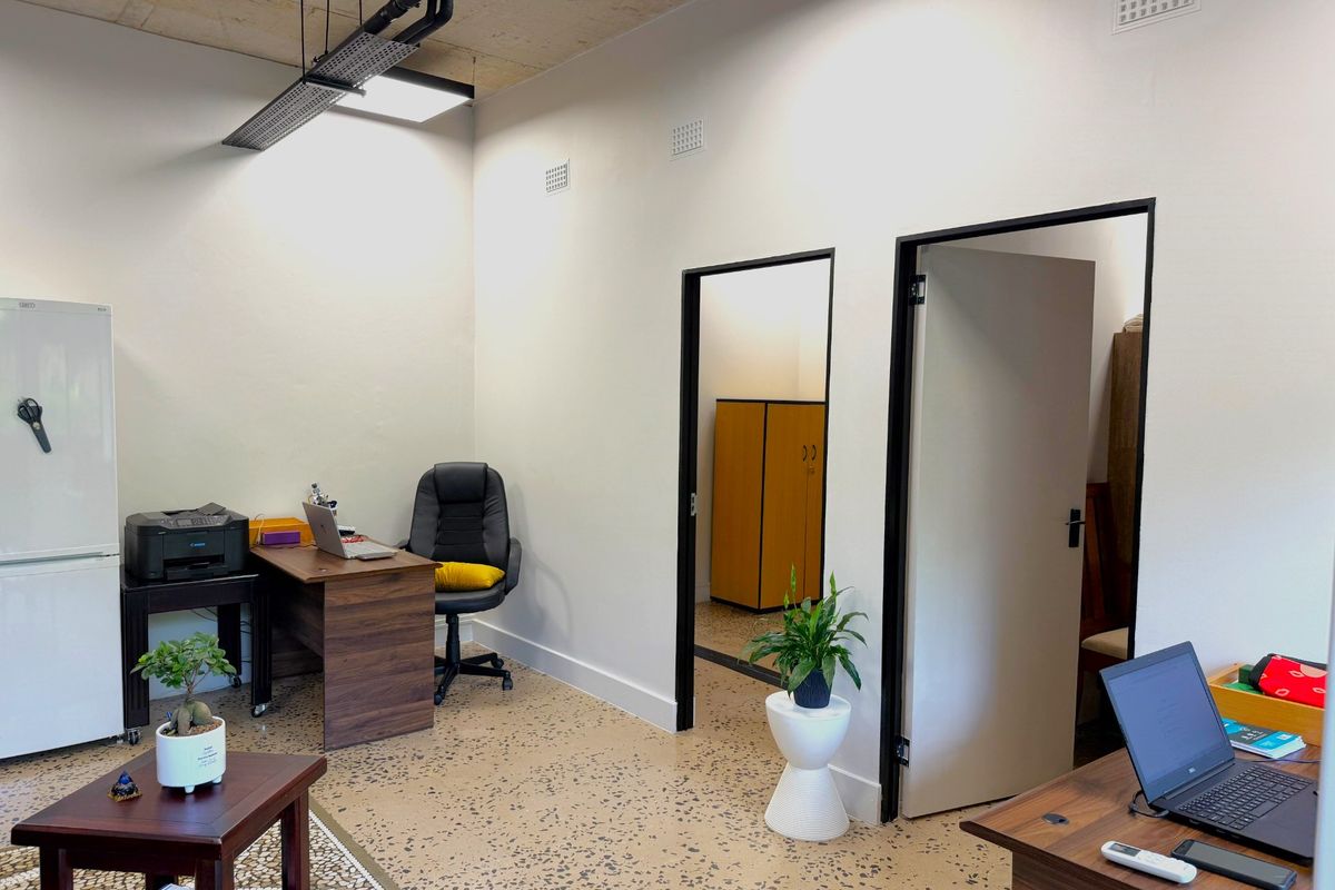 A modern office space featuring exposed concrete ceilings, durable terrazzo flooring, and clean white walls with contrasting black door frames.