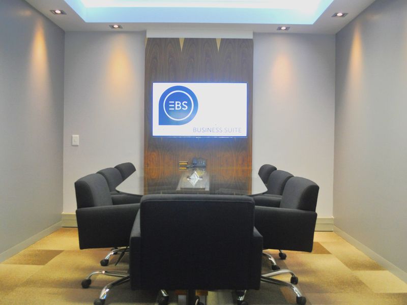 A professional boardroom featuring a wood veneer feature wall with an integrated display screen, recessed ceiling lighting, and cove lighting.