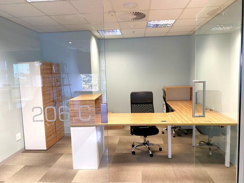 A modern office space featuring glass partition walls, suspended ceiling with recessed lighting, and carpeted flooring.