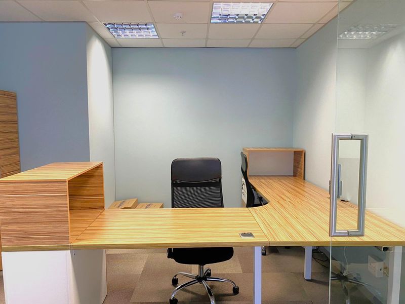 A modern office space featuring a built-in desk, glass partition wall, suspended ceiling with recessed lighting, and professional carpet tiles.