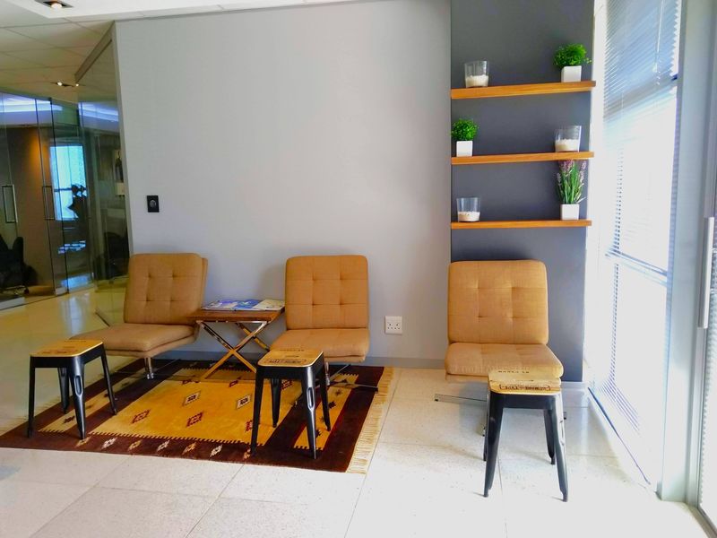 A modern office waiting area featuring built-in wall shelving, tiled flooring, and large windows with venetian blinds, creating a bright and professional atmosphere.