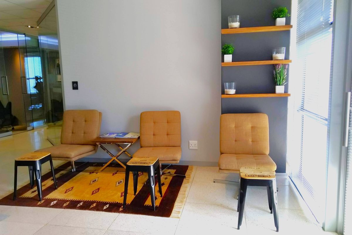 A modern office waiting area featuring built-in wall shelving, tiled flooring, and large windows with venetian blinds, creating a bright and professional atmosphere.