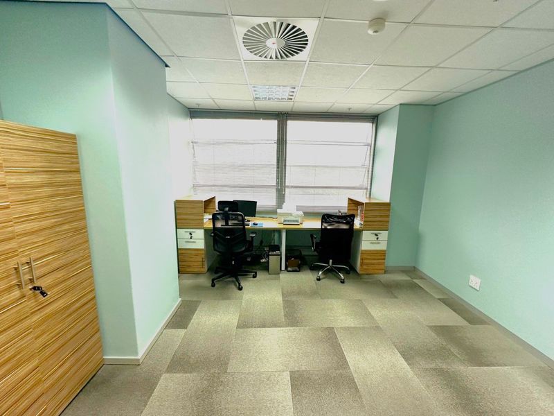 A functional office space featuring carpet tiles, a suspended ceiling with integrated air conditioning, and built-in storage cabinetry.
