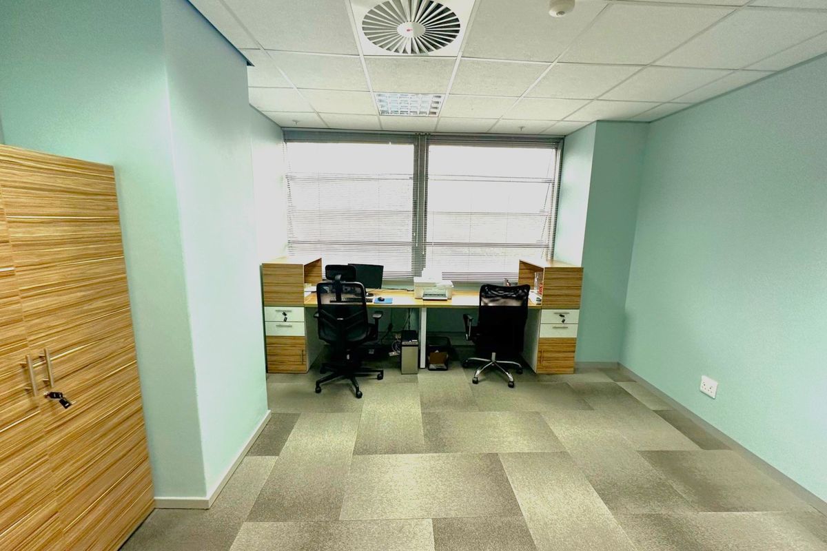 A functional office space featuring carpet tiles, a suspended ceiling with integrated air conditioning, and built-in storage cabinetry.