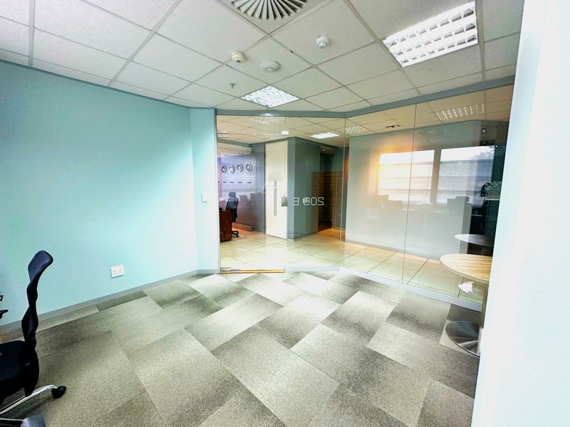 A modern office space featuring a glass partition wall, suspended ceiling with recessed lighting, and durable carpet tiles, offering a professional and bright work environment.