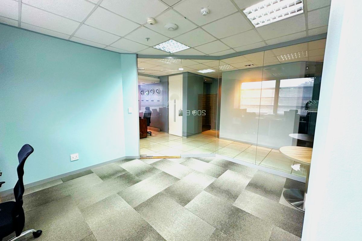 A modern office space featuring a glass partition wall, suspended ceiling with recessed lighting, and durable carpet tiles, offering a professional and bright work environment.