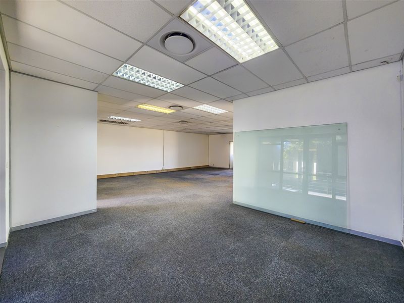 Spacious open-plan office area featuring suspended ceilings, recessed lighting, carpet tiles, and a modern glass partition.