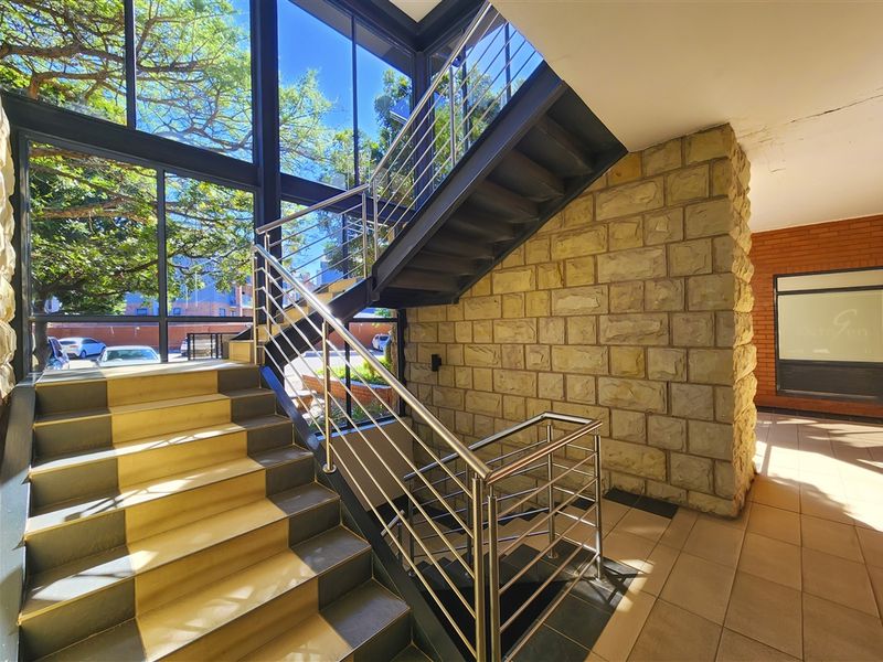 Modern office entrance featuring a striking steel staircase, stone-clad feature wall, and expansive floor-to-ceiling glass windows providing ample natural light.