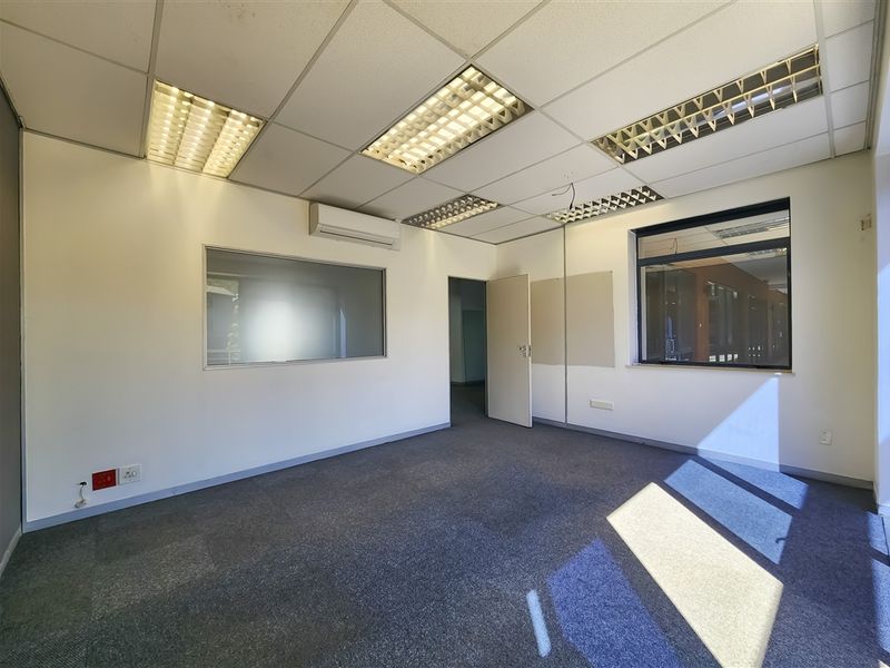 A vacant office space featuring a suspended ceiling with recessed lighting, split-system air conditioning, carpeted flooring, and an internal glass partition.