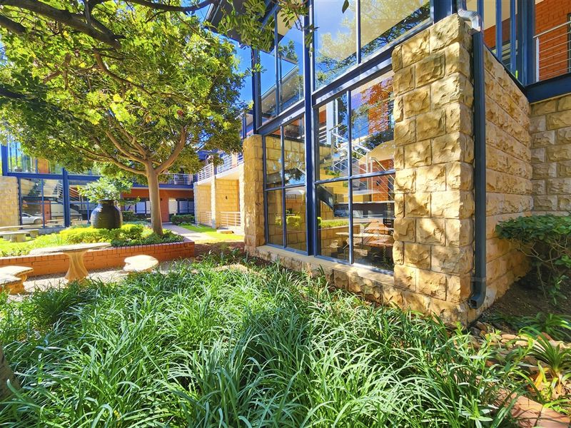 A well-maintained office exterior featuring stone cladding, large glass windows, and a landscaped garden area with mature trees.