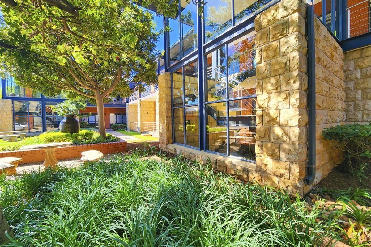 A well-maintained office exterior featuring stone cladding, large glass windows, and a landscaped garden area with mature trees.