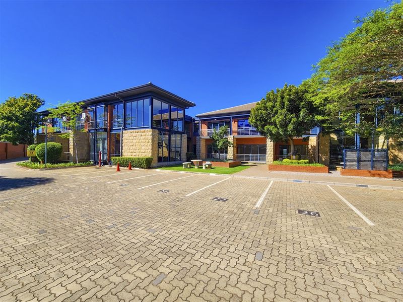 A well-maintained office building exterior featuring stone cladding, large glass windows, and a paved parking area in front.