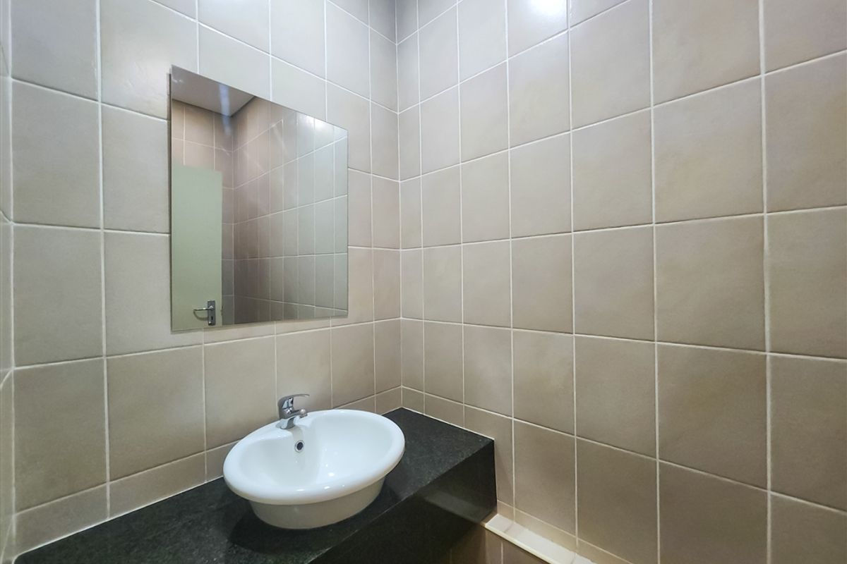A clean, functional office bathroom featuring a ceramic basin set into a granite vanity countertop with wall-to-wall tiling and a mounted mirror.