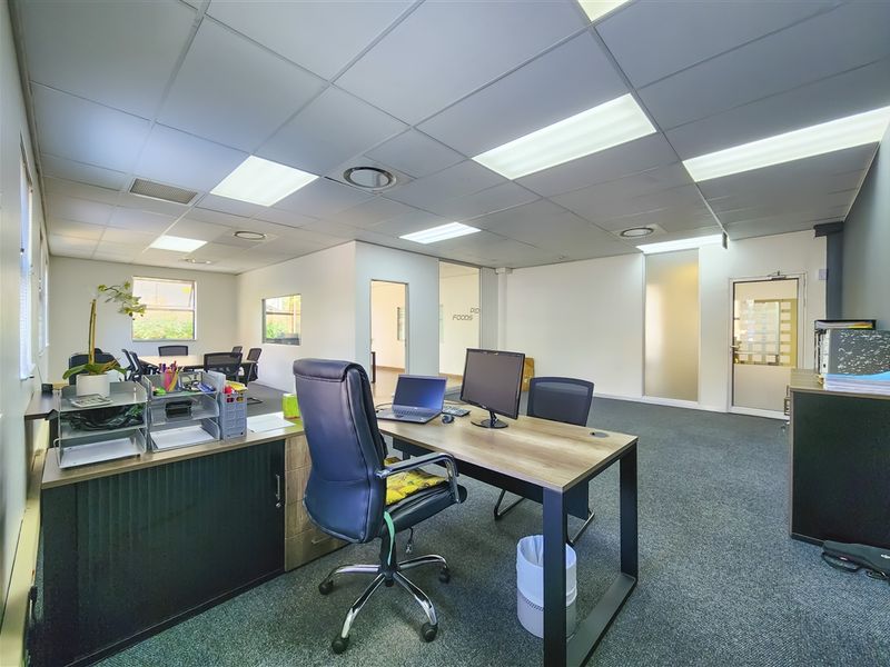 A well-lit open-plan office space featuring a suspended ceiling, recessed lighting, and carpeted flooring with a glass partition door.