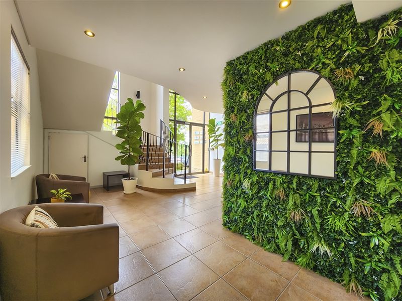 A bright and welcoming office entrance featuring tiled flooring, a decorative green feature wall, and a staircase with a wrought iron balustrade.