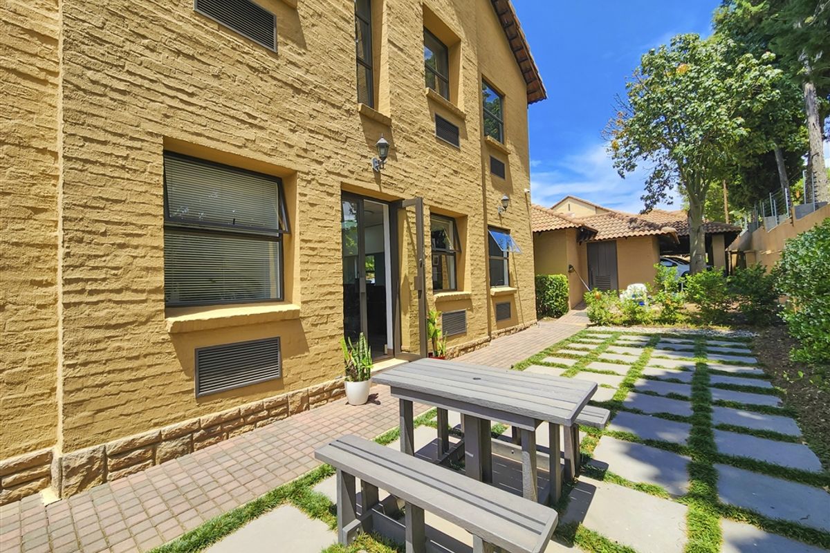 Rear exterior view of the office building featuring a textured brick facade, paved patio area, and a landscaped stone pathway.