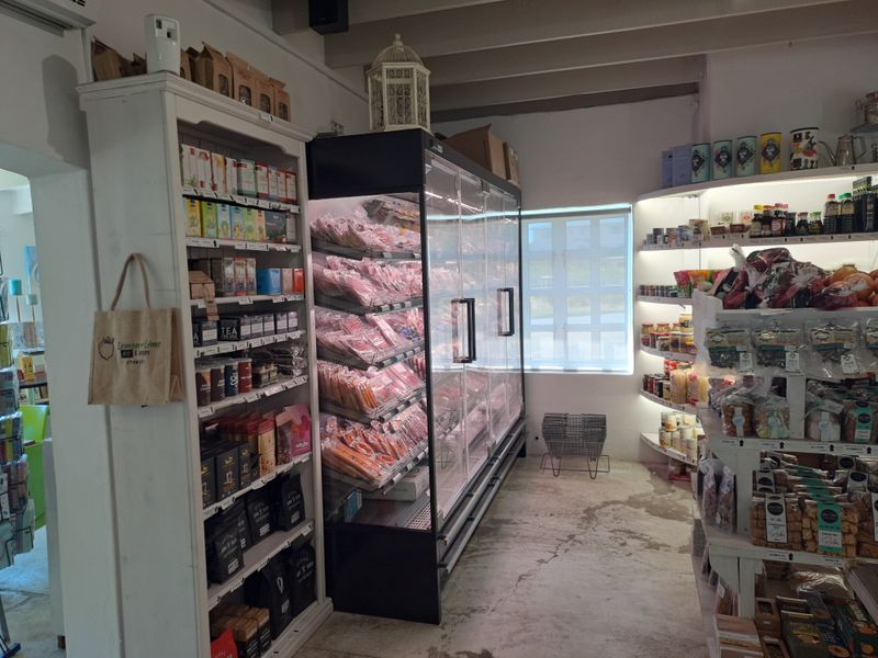 A commercial retail space featuring built-in shelving units, a large glass-fronted commercial refrigerator, and exposed ceiling beams with concrete flooring.
