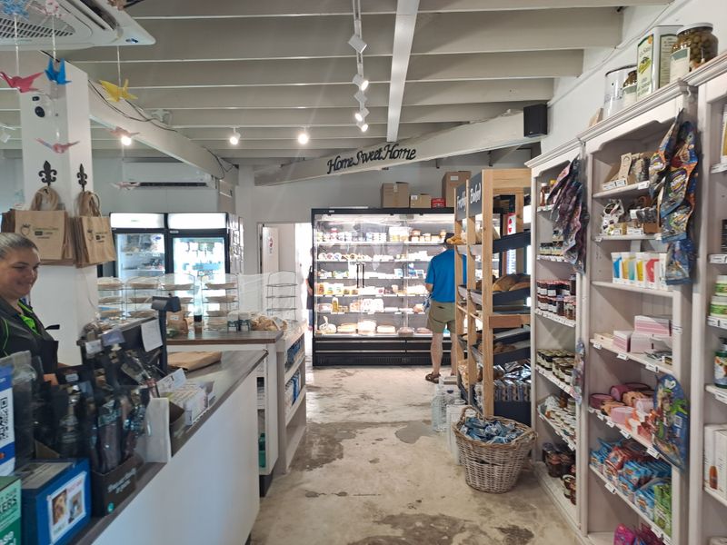 A commercial retail kitchen space featuring built-in shelving, commercial refrigeration units, and exposed beam ceilings with track lighting.