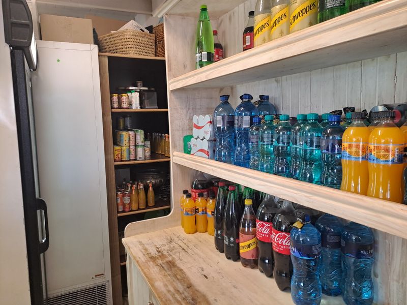 A functional scullery or storage area featuring built-in wooden shelving units and a commercial upright refrigerator for beverage storage.