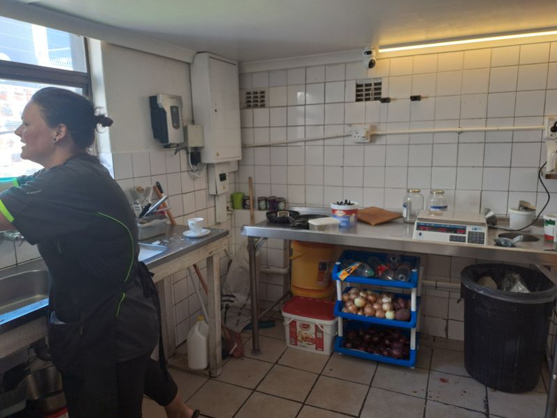 A functional commercial kitchen area featuring stainless steel prep surfaces, tiled walls, and basic utility infrastructure for food preparation.