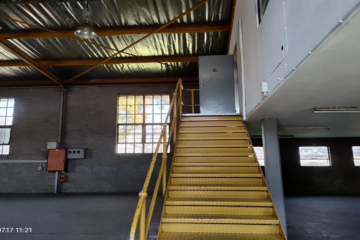 Spacious industrial utility area featuring exposed steel roof trusses, brick walls, and a prominent yellow metal staircase leading to an upper level.