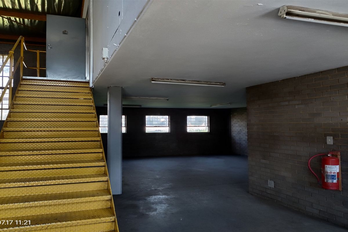 Industrial utility space featuring a yellow metal staircase, exposed brick walls, concrete flooring, and functional overhead fluorescent lighting.