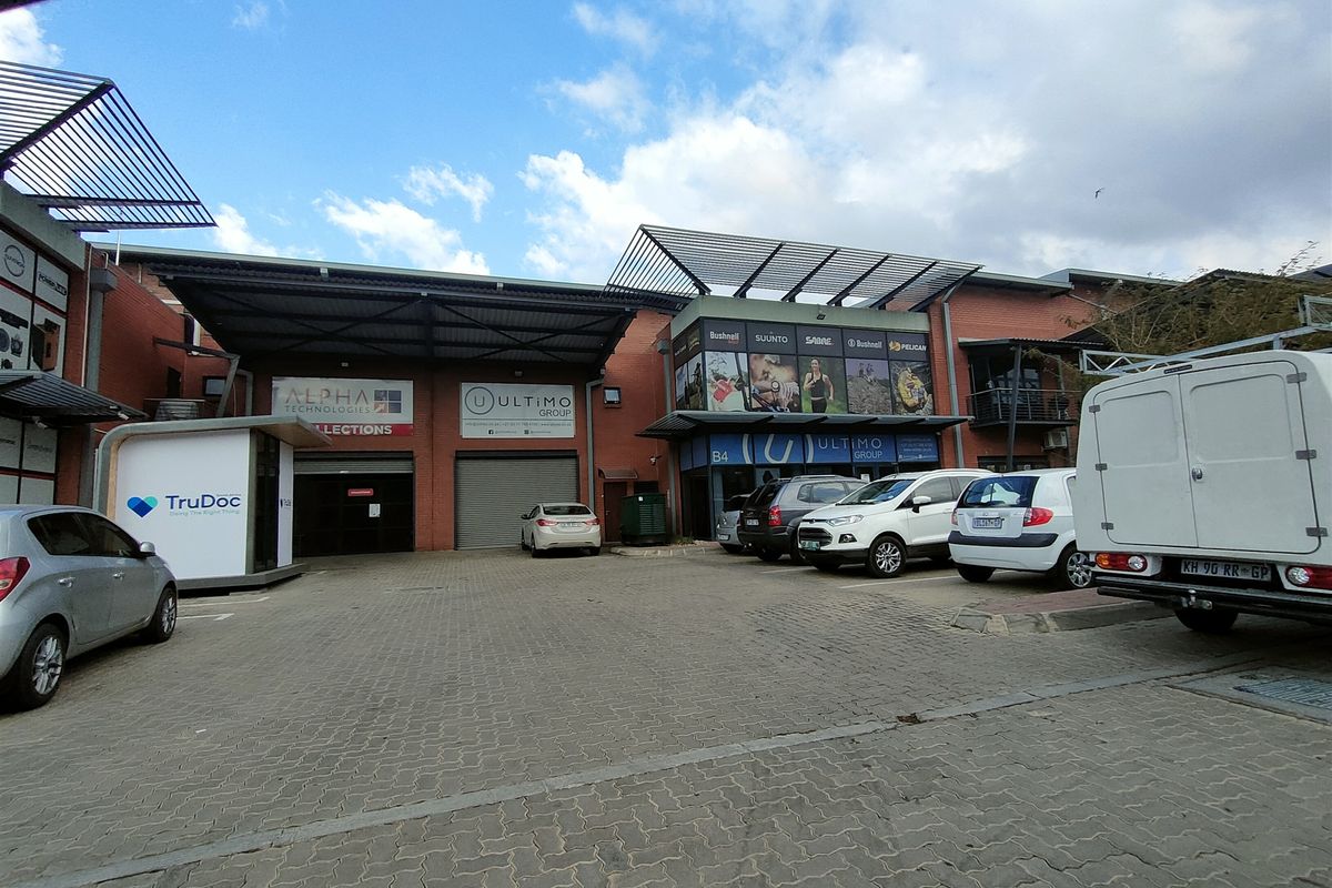 Front view of an industrial property featuring a paved driveway, roller shutter doors, and brick facade with commercial signage.