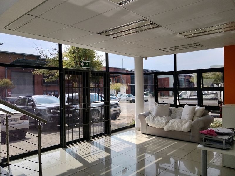 Bright industrial entry area featuring floor-to-ceiling glass windows, tiled flooring, and a suspended ceiling with integrated lighting, providing a professional and welcoming reception space.