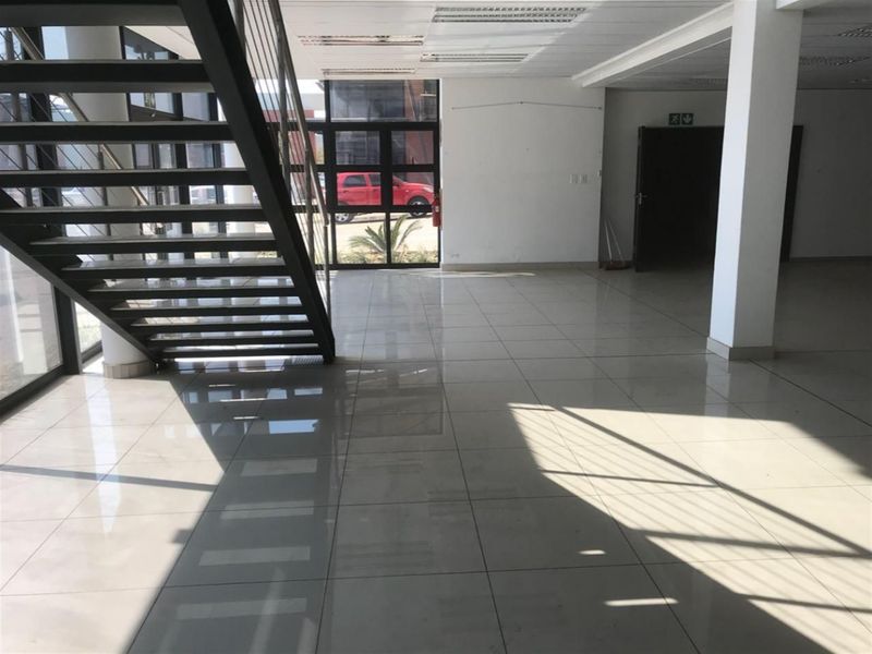 Spacious industrial entrance area featuring polished tiled flooring, a modern metal staircase, and large glass windows providing ample natural light.