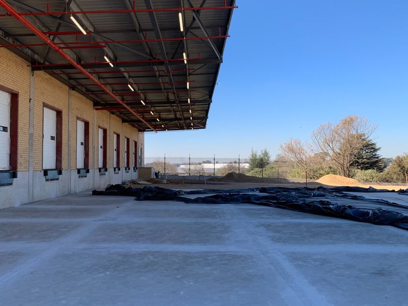 Industrial loading bay area featuring multiple roller shutter doors, overhead sprinkler system, and a large concrete yard under a steel canopy.