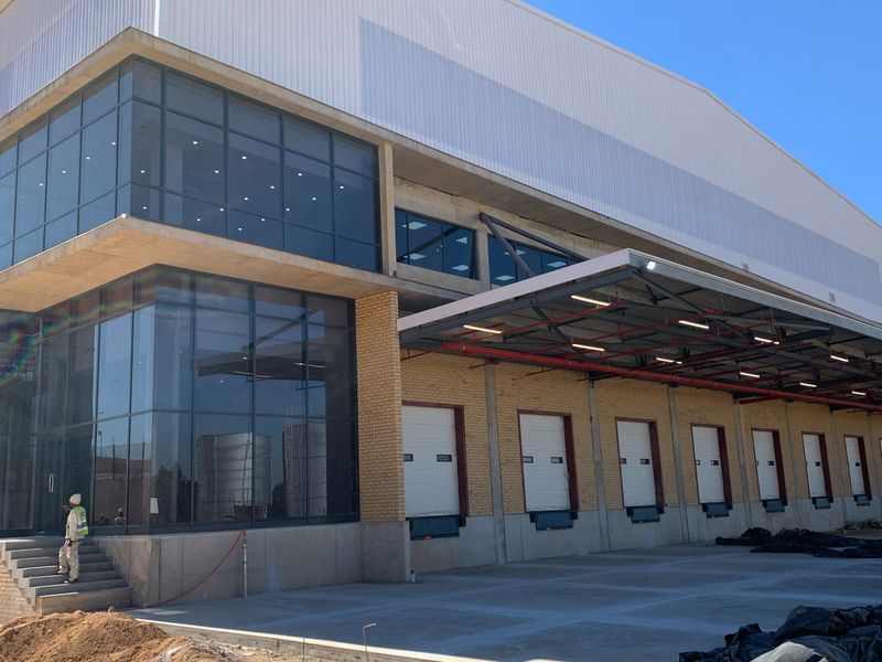 Modern industrial warehouse facility featuring multiple loading docks with roller shutter doors, a large steel canopy, and extensive glass curtain walling.