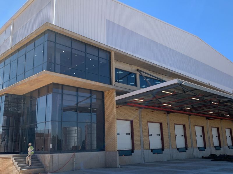 Modern industrial warehouse facility featuring a large loading bay area with multiple roller shutter doors, glass curtain walling, and a covered loading canopy.