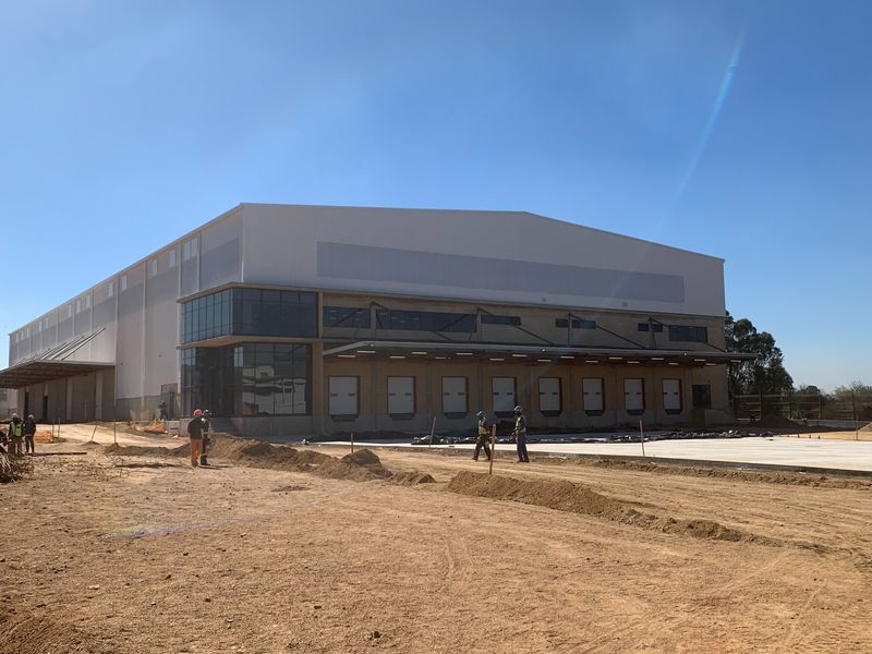 Industrial warehouse facility featuring multiple loading docks, modern curtain wall glazing, and a large concrete yard area currently under final construction.