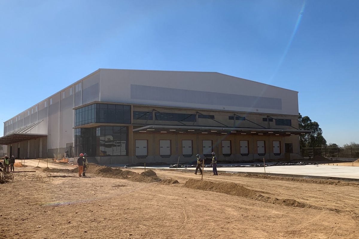 Industrial warehouse facility featuring multiple loading docks, modern curtain wall glazing, and a large concrete yard area currently under final construction.