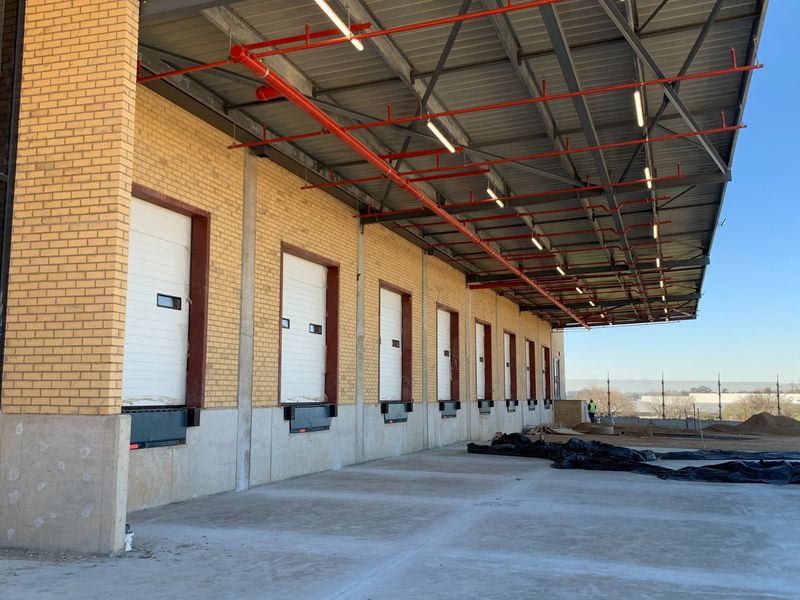 Industrial loading bay area featuring multiple dock doors, overhead sprinkler system, and a large covered concrete apron for efficient logistics operations.