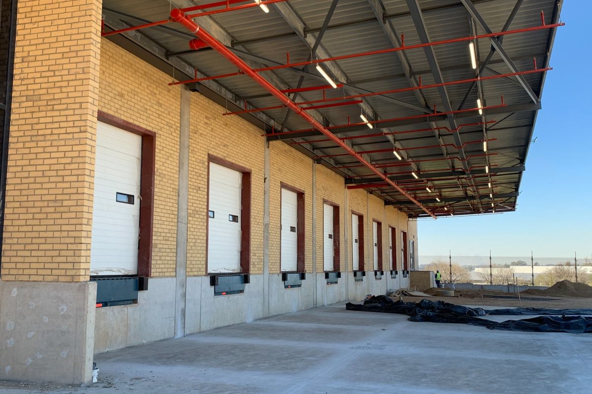 Industrial loading bay area featuring multiple dock doors, overhead sprinkler system, and a large covered concrete apron for efficient logistics operations.