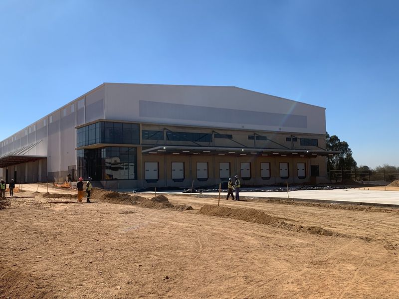 A modern industrial warehouse facility featuring multiple loading docks, extensive metal cladding, and large glass facade elements under construction.
