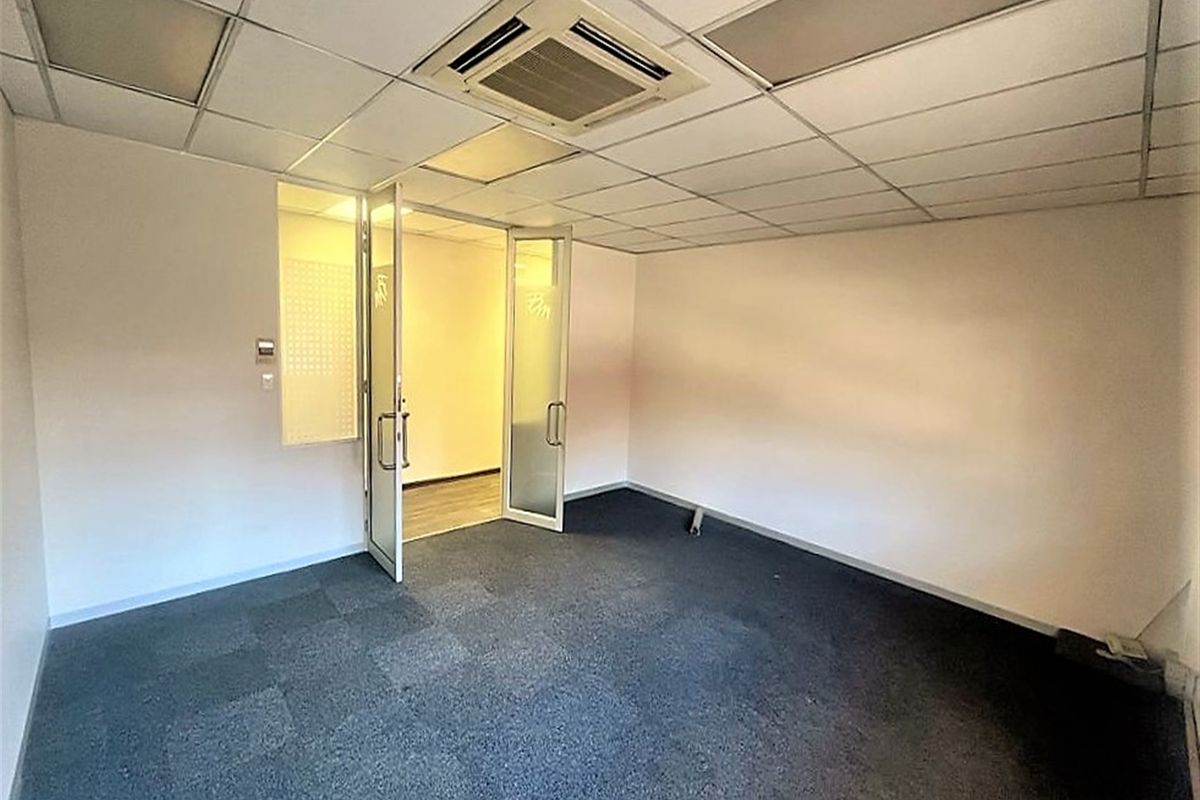 A vacant office space featuring a suspended ceiling with integrated air conditioning, carpeted flooring, and glass panel doors leading to an adjacent room.