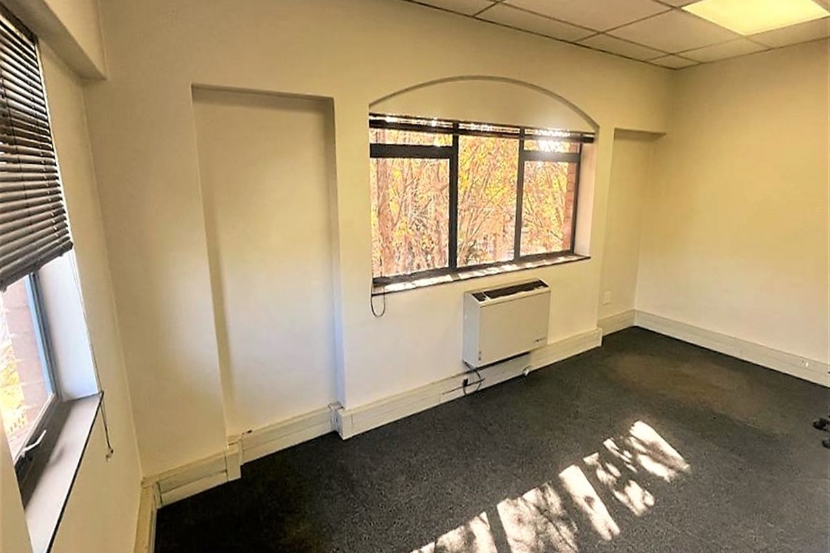 A vacant office space featuring carpeted flooring, a suspended ceiling with recessed lighting, and a wall-mounted HVAC unit.