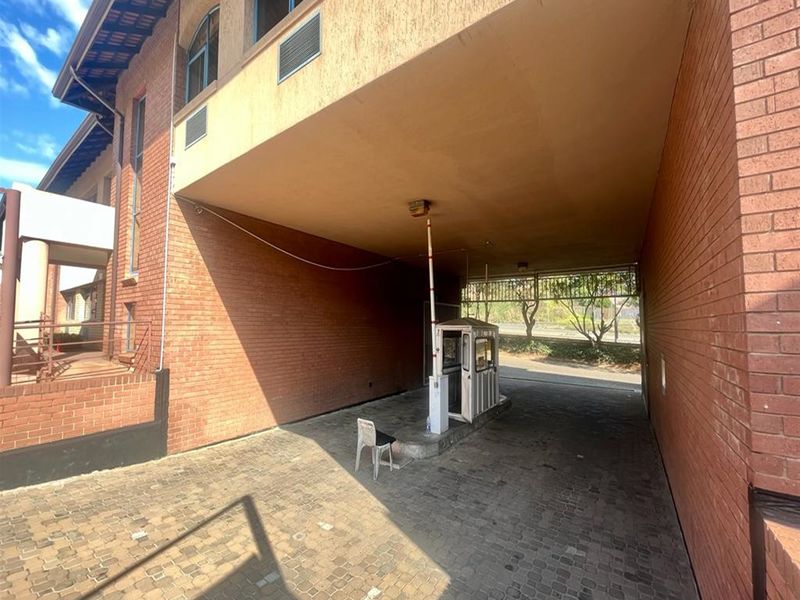 A covered office building entrance featuring a brick facade, paved driveway, and a dedicated security guard booth with a boom gate.