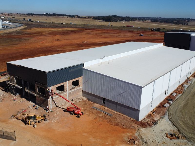 Aerial view of an industrial warehouse facility currently under construction, featuring metal roofing, steel cladding, and ongoing exterior brickwork.