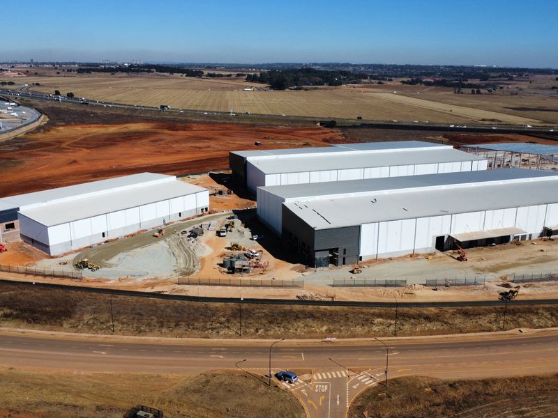 Aerial view of a large-scale industrial development site featuring multiple warehouse structures under construction with surrounding access roads and open land.