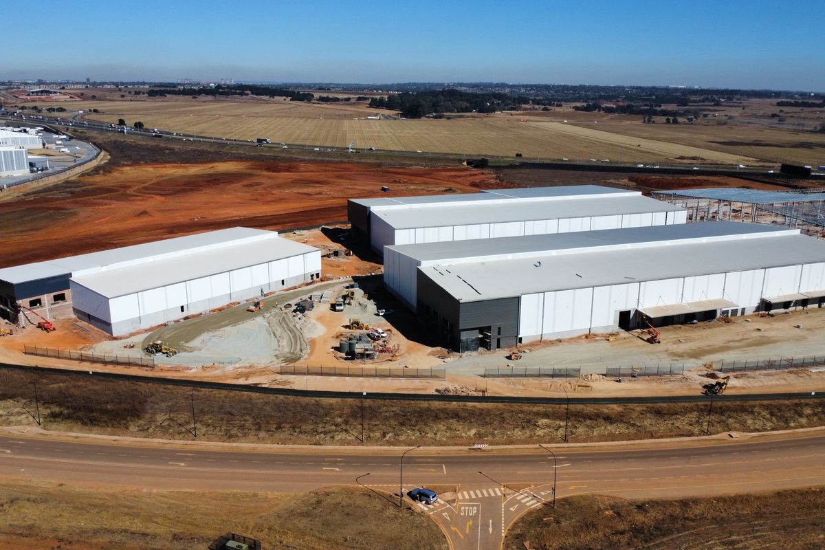 Aerial view of a large-scale industrial development site featuring multiple warehouse structures under construction with surrounding access roads and open land.