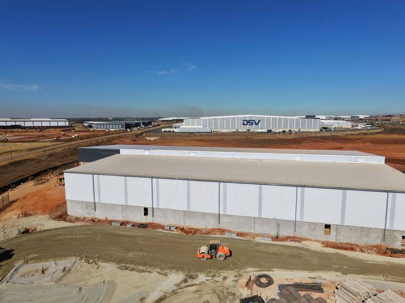 Aerial view of a large industrial warehouse facility under construction, featuring metal cladding and expansive surrounding site development.