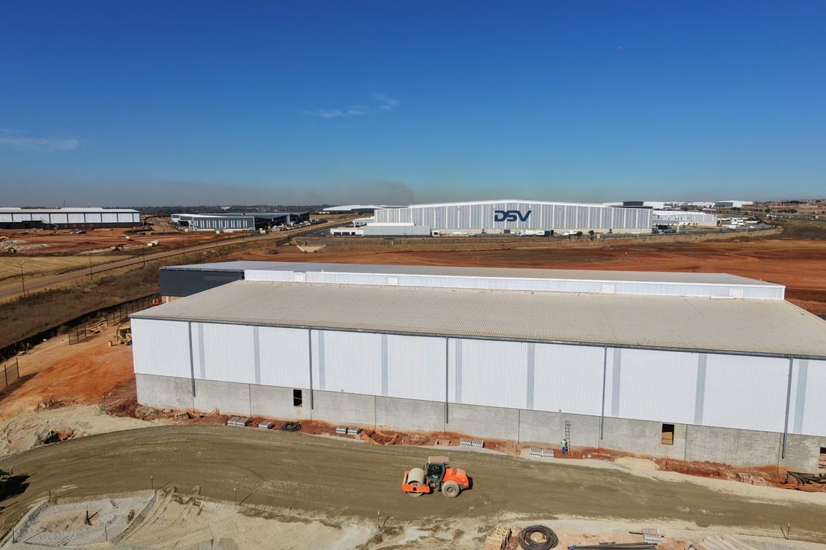 Aerial view of a large industrial warehouse facility under construction, featuring metal cladding and expansive surrounding site development.