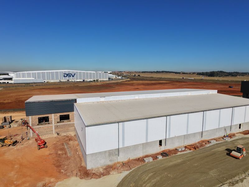Aerial view of an industrial warehouse facility under construction, featuring metal cladding, concrete foundations, and surrounding site development.