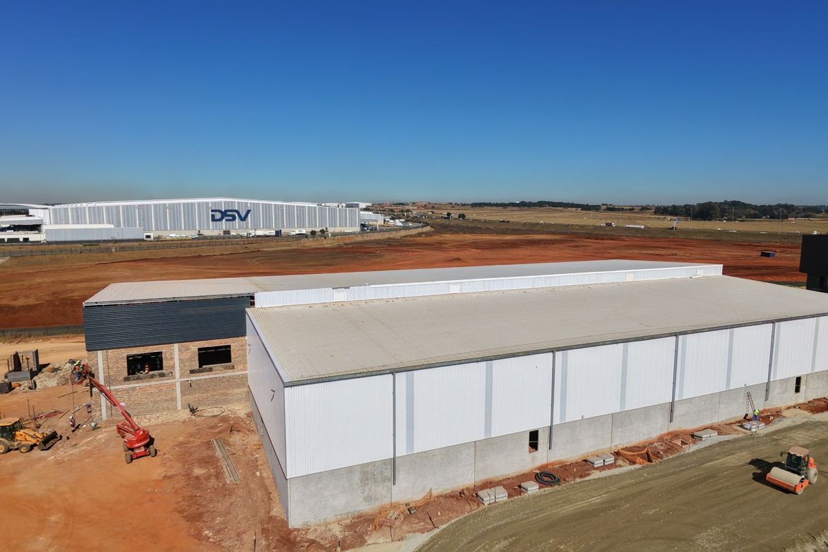 Aerial view of an industrial warehouse facility under construction, featuring metal cladding, concrete foundations, and surrounding site development.